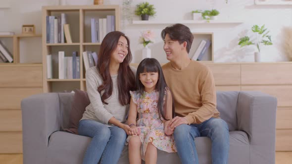 Happy Asian family sitting on couch smile with love and looking at camera spend time together.Father