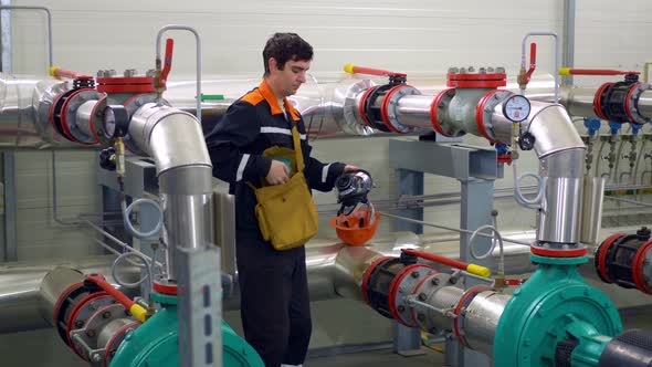 A Chemical Worker Puts on a Gas Mask in Front of Pipes with Pesticides