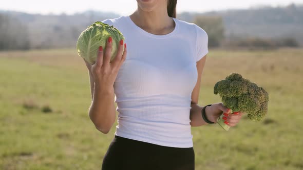 Girl Stands On The Field With Cabbage And Broccoli In Her Hands