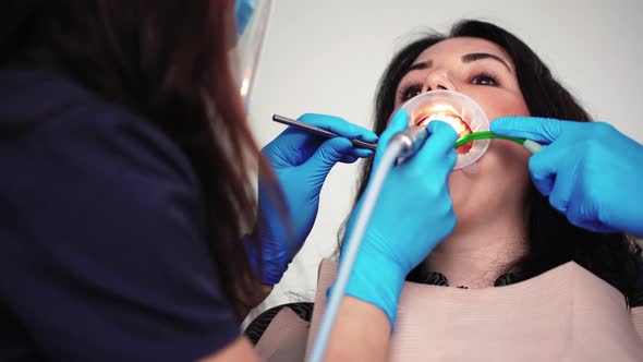 Woman Dentist with Assistant Does Brushing Teeth Female Patient in Dental Clinic