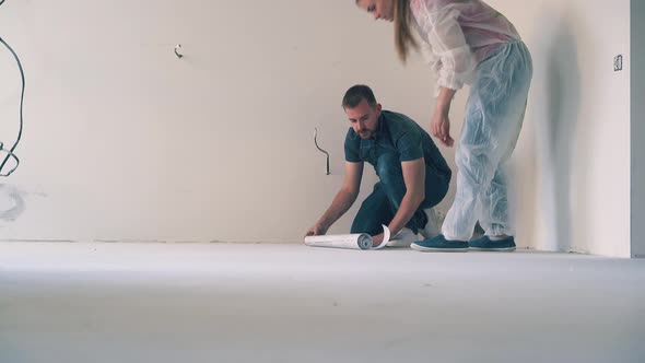 Man with Wife Checks Sheet of Wallpaper on Floor Near Wall