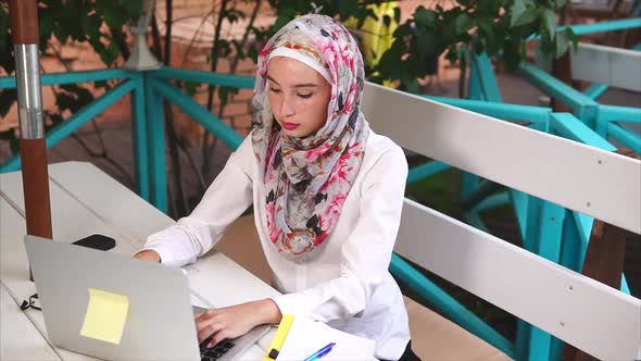 A Modern Muslim Woman in a Hijab Prints a Letter To a Business Partner on Laptop