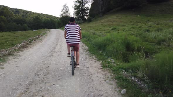 Close up shot of male cyclist filmed from behind on a country road. Man in casual summer clothes rid