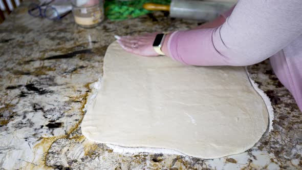 Squaring up the sides of rolled out dough to make cinnamon rolls - isolated side view