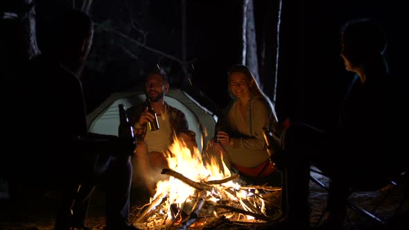 Group of Friends Drinking Beer Near Bonfire, Tent Camp, Friendly Atmosphere