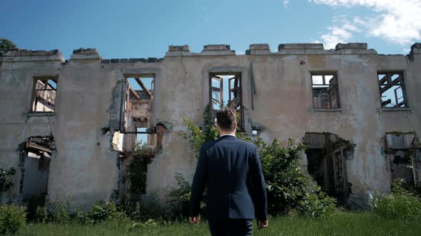 Successful man in a jacket goes to an abandoned ruined house