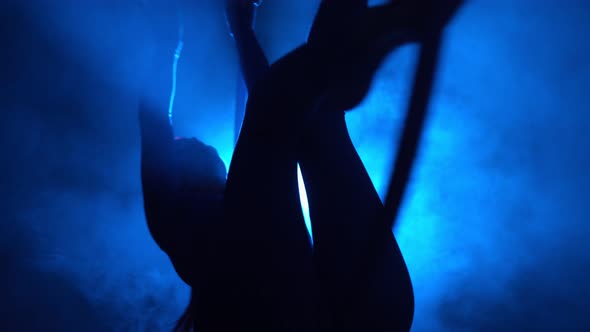 Silhouette Aerial Gymnast Performs Trick in Ring in Smoky Room with Backlit