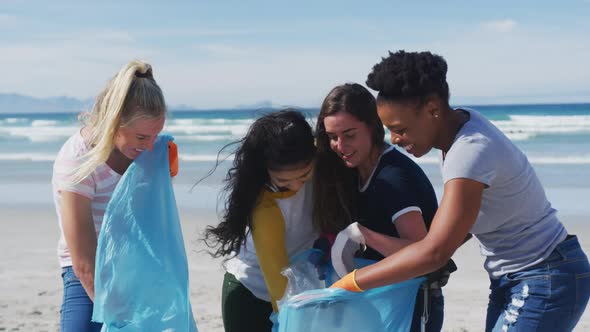 Diverse group of female friends putting rubbish in refuse sacks at the beach