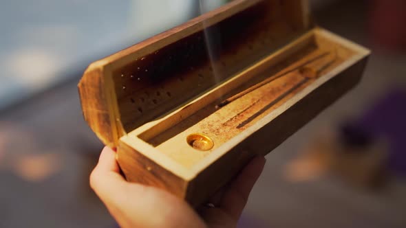 Hand holding a wooden box with burning incense during sunset light in yoga studio. Close up, slow mo