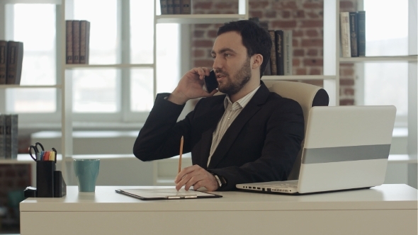 Man Talking On Mobile Phone While Using Laptop