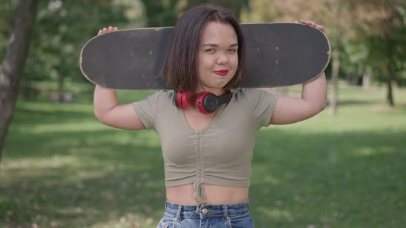 Cute Little Woman Holding Skateboard on Shoulders Smiling Looking at Camera