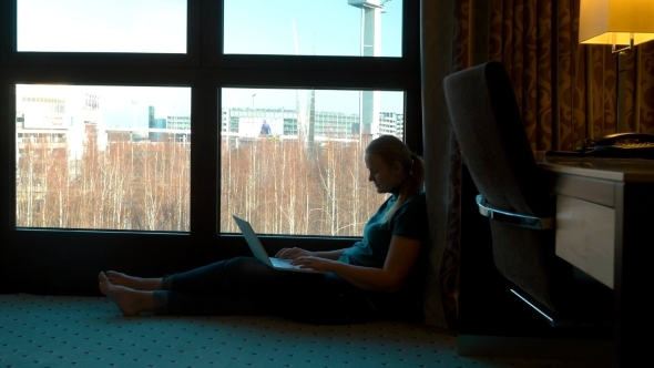 Woman Uisng Laptop By The Window In Hotel Room