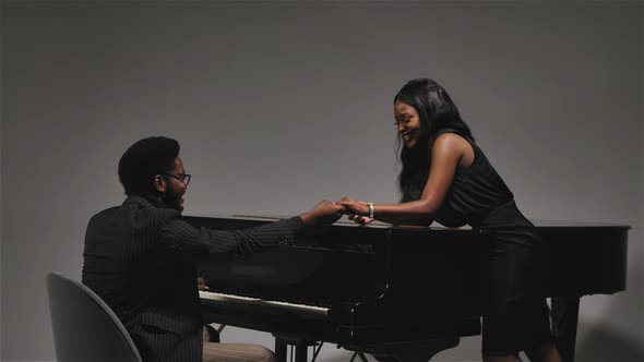 Happy Young African American Couple Hold Hands Near a Black Piano and Smile at Each Other