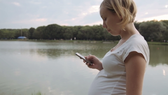 Pregnant Woman Using Mobile Phone In Park