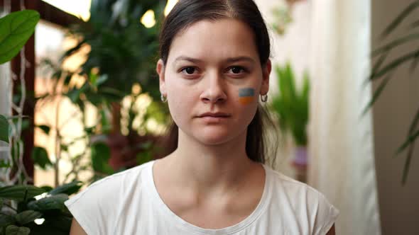 Young Sad Ukrainian Girl with the Flag of Ukraine and Russia on Her Face is Closing Her Eyes