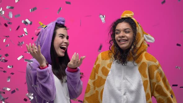 Excited Women in Funny Animals Pajamas Standing Under Confetti Shower, Hugging