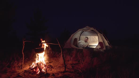 A Man Rests in a Tent Near a Fire