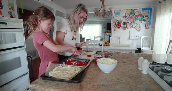 A mother and daughter have a great time putting together a homemade pizza.