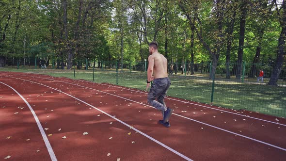 Sport man running on racetrack. View of athletic shirtless sportsman running on track