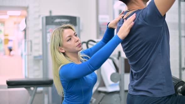 Young woman trainer monitors the correctness of the exercise by the man