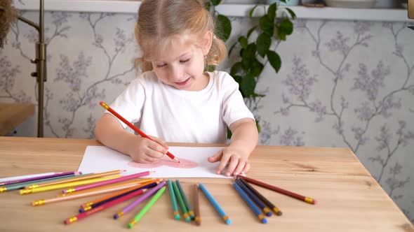 a Little Girl Enthusiastically Draws a Heart with Colored Pencils Sitting at the Table at Home Alone