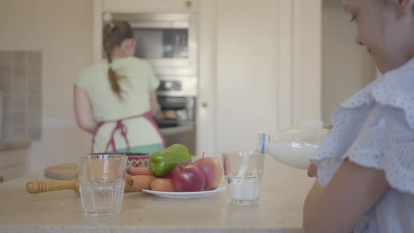 Daughter Pouring Milk Into a Glass, and Happy Mom Pulling Out Freshly Baked Buns From the Oven