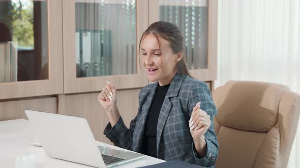 Happy businesswoman working with laptop computer and dancing while sitting at desk she successful