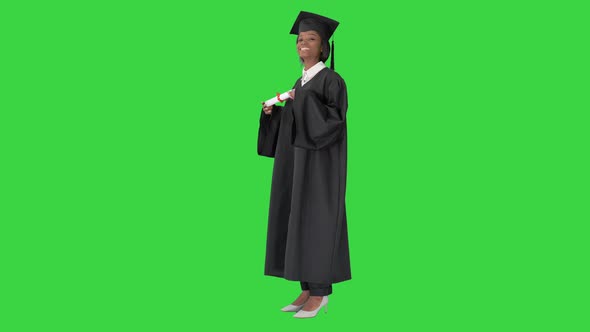 Smiling African American Female Student in Graduation Robe Posing with Diploma on a Green Screen