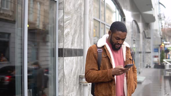 Black Man with Shoulder Backpack Stands Outdoor Near the Office Center