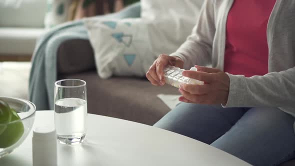 Mature Woman Taking Pill in Hand Sitting on Sofa in Home Room.