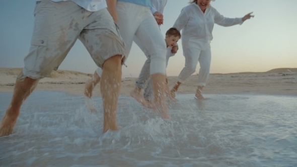 Family Walking On The Beach And Splashing Water