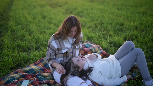 Loving tender mum with a cute daughter sitting on a blanket on a field