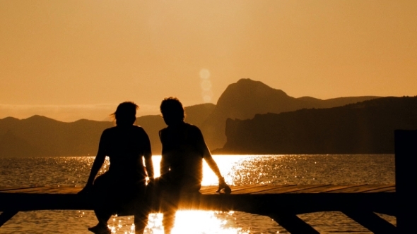 Young Couple Sitting On Bridge At Sunset