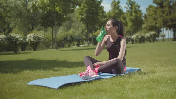 Fit Asian Woman Sipping Energy Drink on Finess Mat