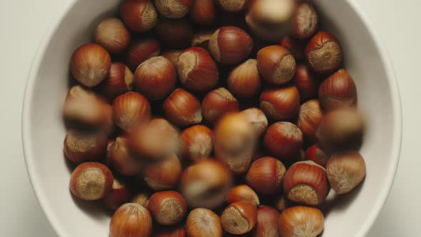 Inshell hazelnuts falling into a white bowl