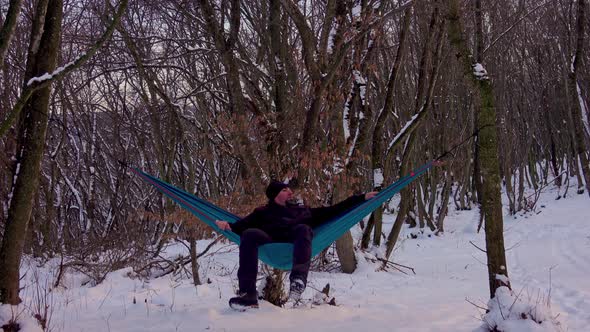 Man lying in hammock under the trees in the winter forest
