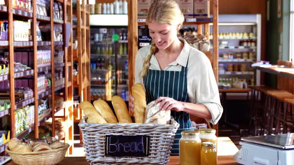 Smiling female staff checking loaf of bread at bread counter