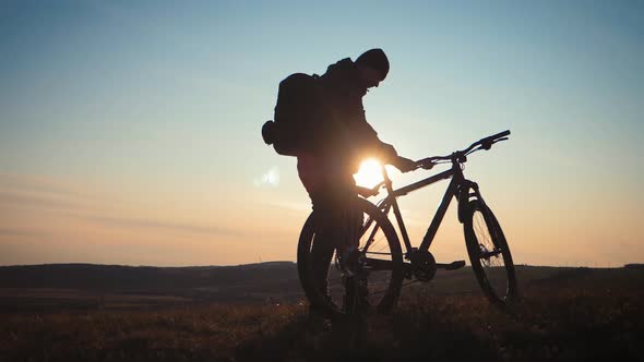 The Silhouette of the Mountain Bicycle Rider on the Hill with Bike at Sunset. Sport, Travel and