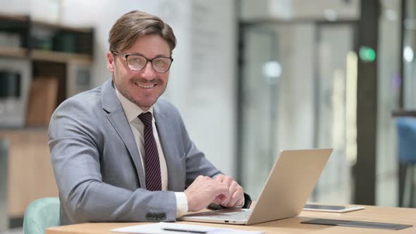 Businessman with Laptop Smiling at Camera in Office 