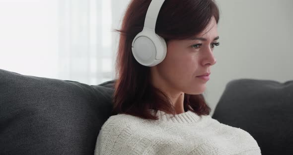 Portrait of Beautiful Woman Listening Music in Wireless Headphones While Relaxing on Grey Couch