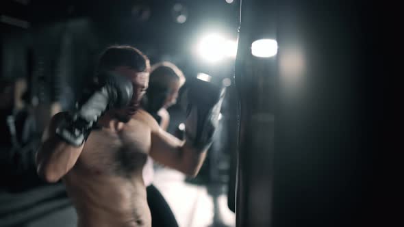 A Muscular Man and Woman are Hits Punching Bag in the Gym