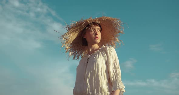 Blonde Caucasian Girl standing on Field in Straw Hat and looking at Sun