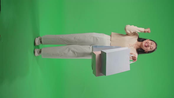 Full View Of Happy Woman Holding Shopping Bags Up While Standing In Front Of Green Screen