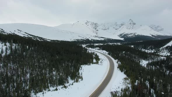 Aerial footage of black forest, white rocky mountains, winter road (Alberta, Canada)