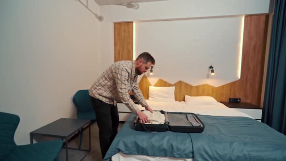 a young man takes out his clothes from a suitcase in a hotel room