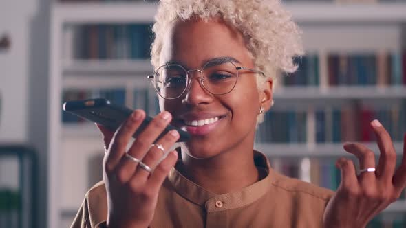 Happy Young African American Woman Dictating Voice Message in Mobile Phone