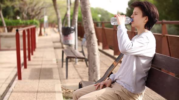 Tired Teenage Girl Sitting on Chair and Drinking Water From the Bottle