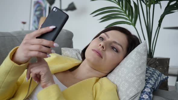 Woman Using Smartphone in Shock Wondering While Laying on Sofa