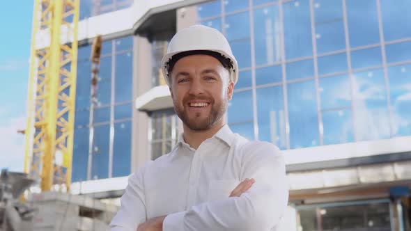 An Engineer in a White Shirt and Helmet Stands Against the Backdrop of a Modern Glass Building