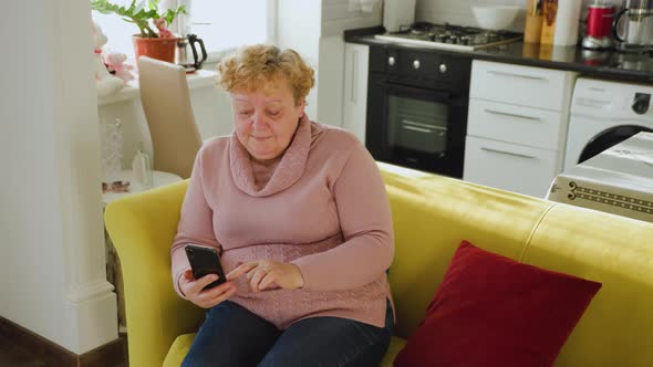 Senior Lady Using Smartphone Surfing the Net Sit on Couch at Home in the Living Room